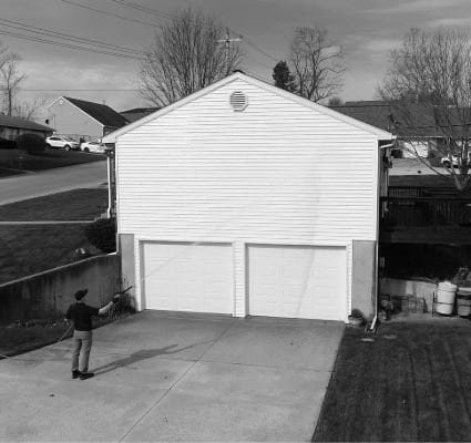 A man power washes a two-car garage. This Coronado Window Cleaning project shows a residential building with white siding and two garage doors, highlighting exterior home maintenance.