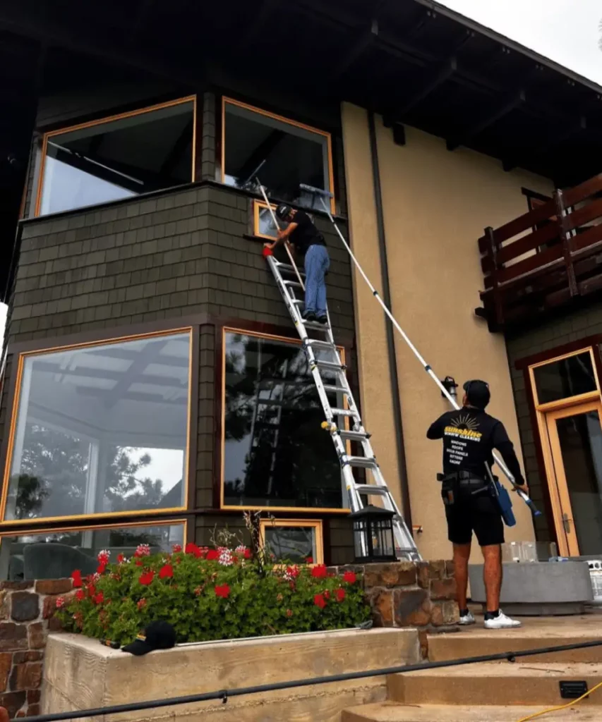 Two window cleaners working on a high-end home in Point Loma. One is on a ladder cleaning upper windows, the other uses a water-fed pole for advanced window cleaning on lower windows.