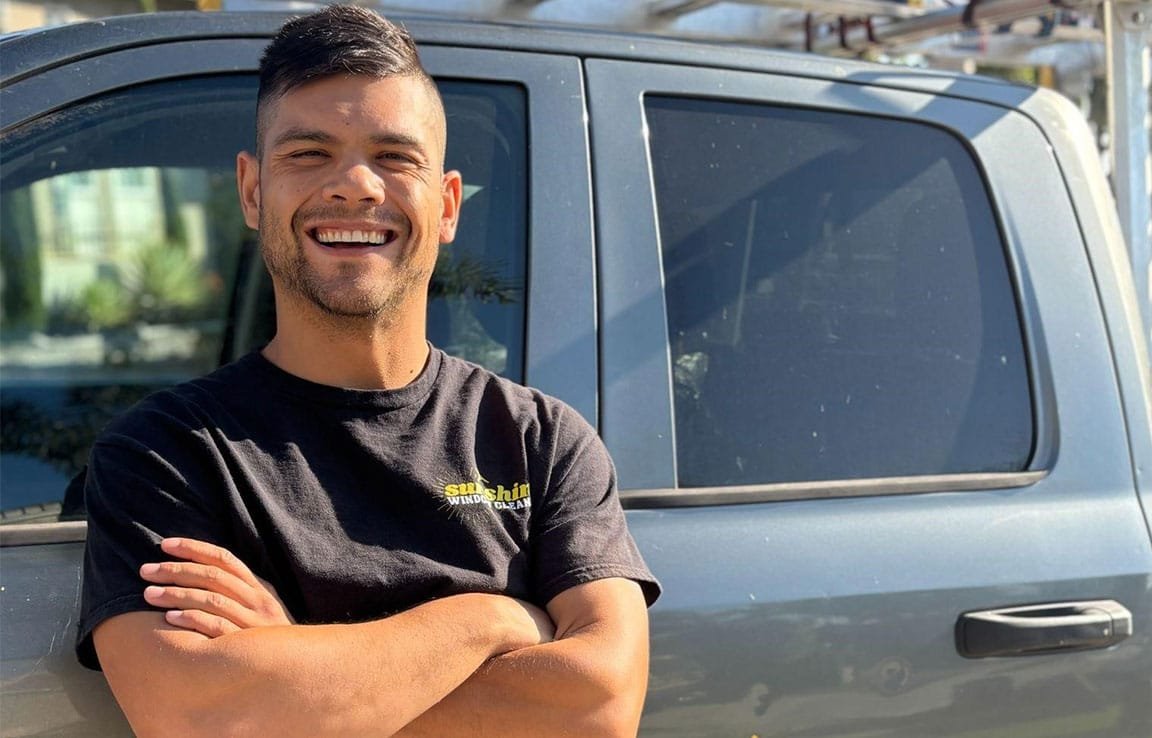 Smiling window cleaner in San Diego stands proudly in front of his work truck, ready to help you clean your gutters. His shirt reads "Sunshine Window Clean.